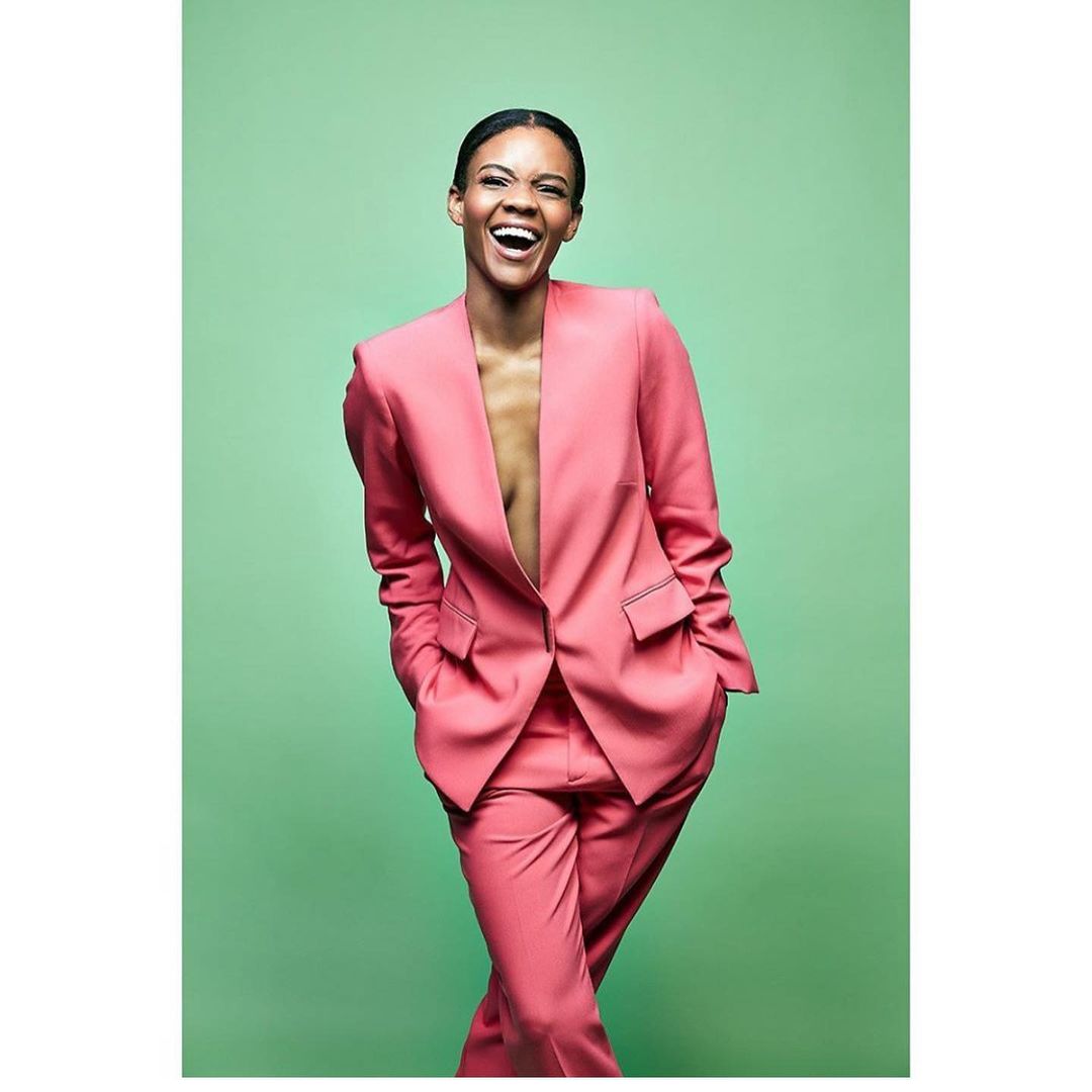 A photo showing Candace Owens in a pink suit and pant, with a cute smile on her face.