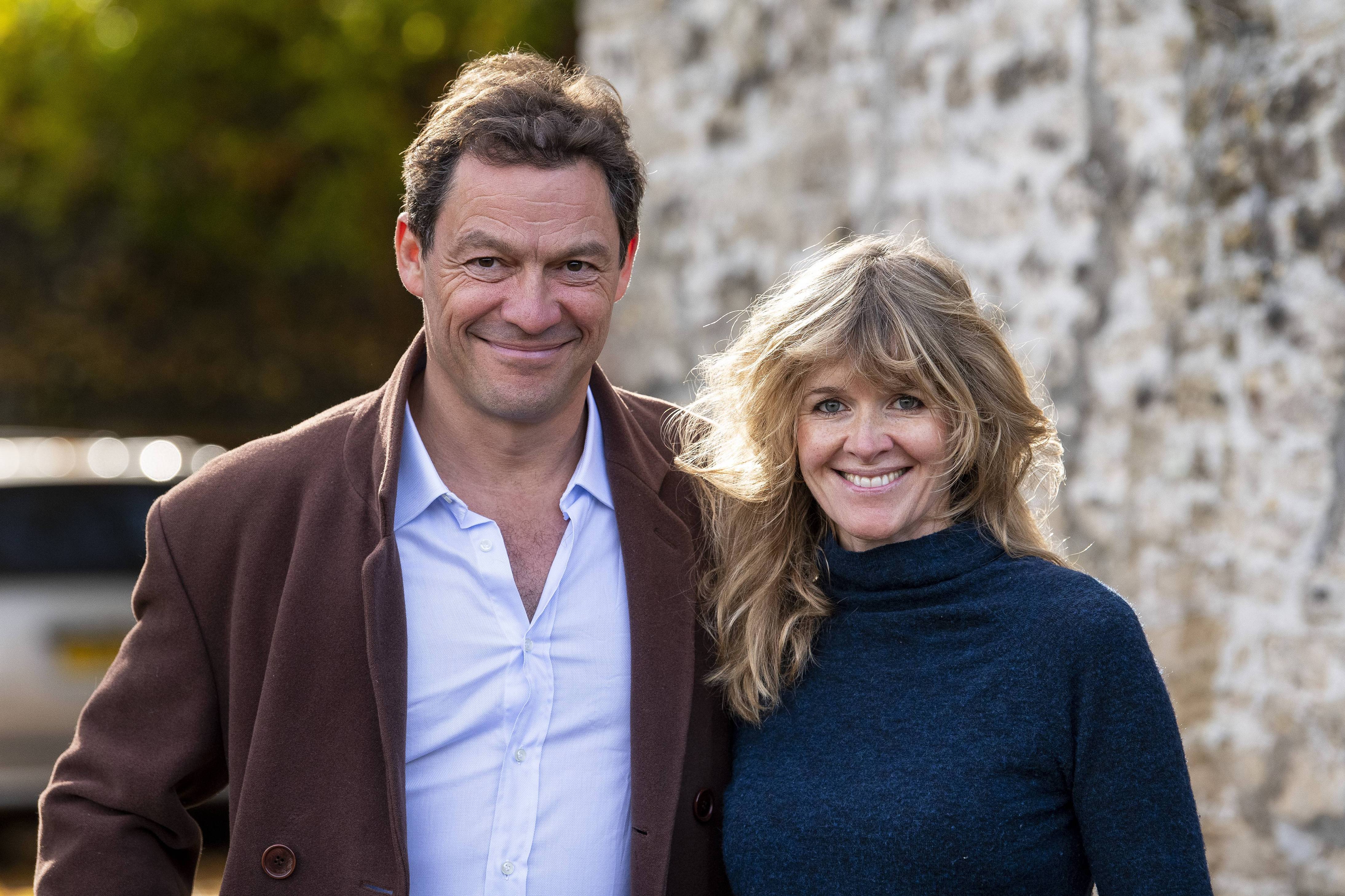 A photo of Dominic West and wife, Catherine FitzGerald smiling beautifully for the camera outside their home.