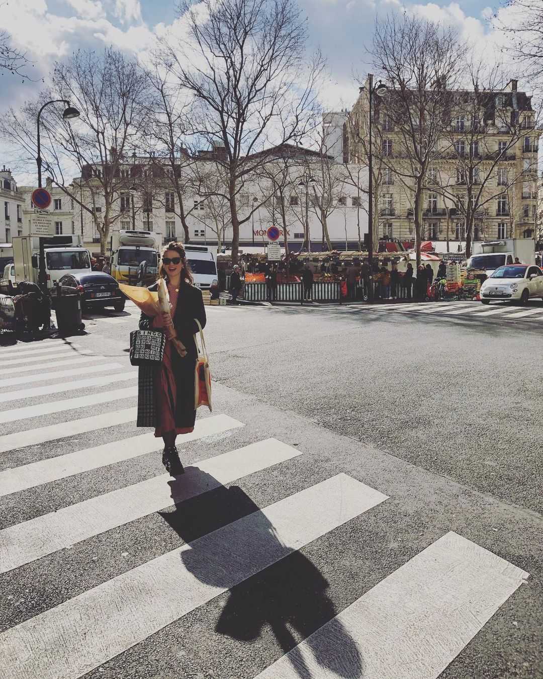 Lily James, sporting a long black jacket in on the street, carrying two handbags and cartons.