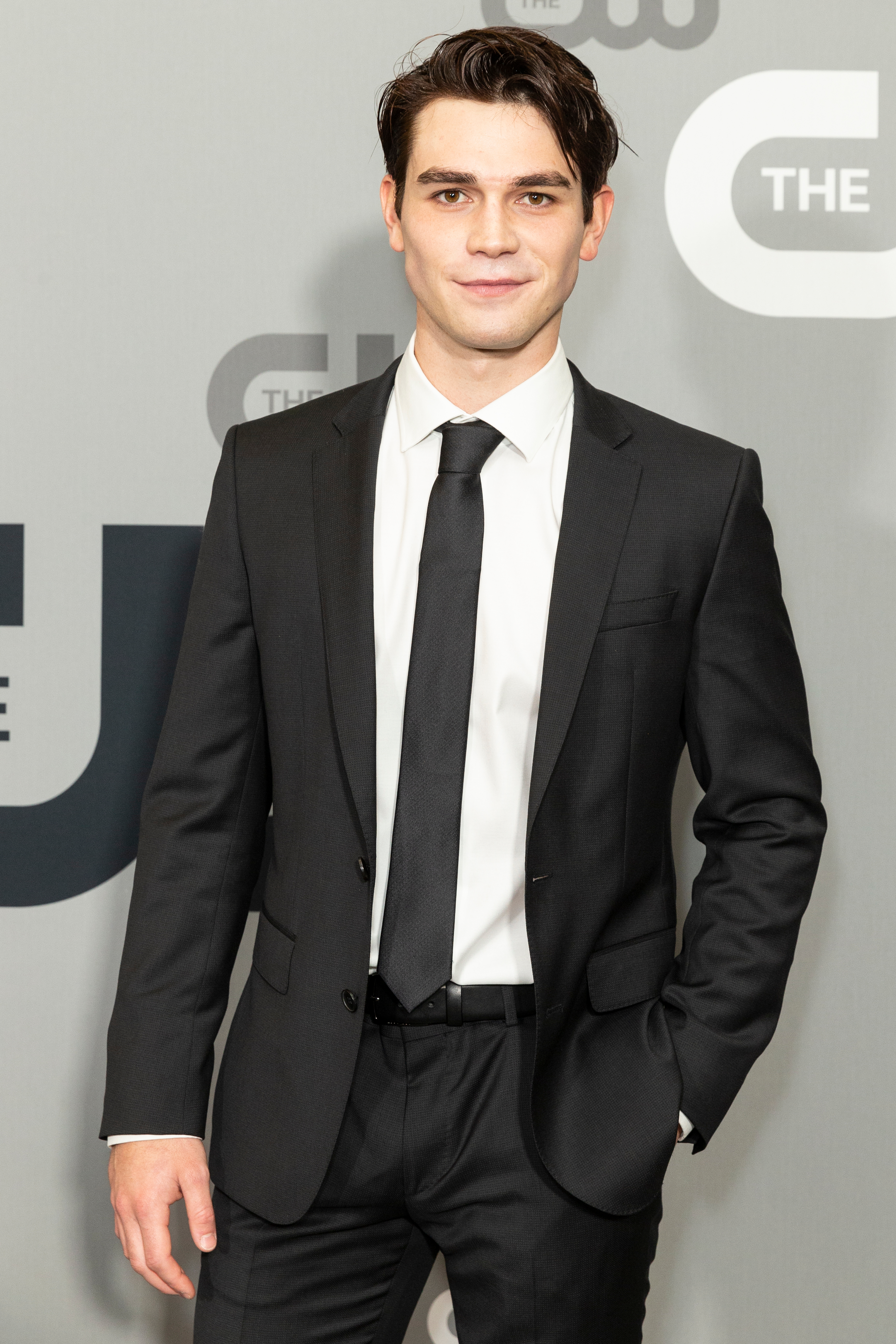 An amazing photo showing KJ Apa in a black tux with a white inner T-shirt and black tie.