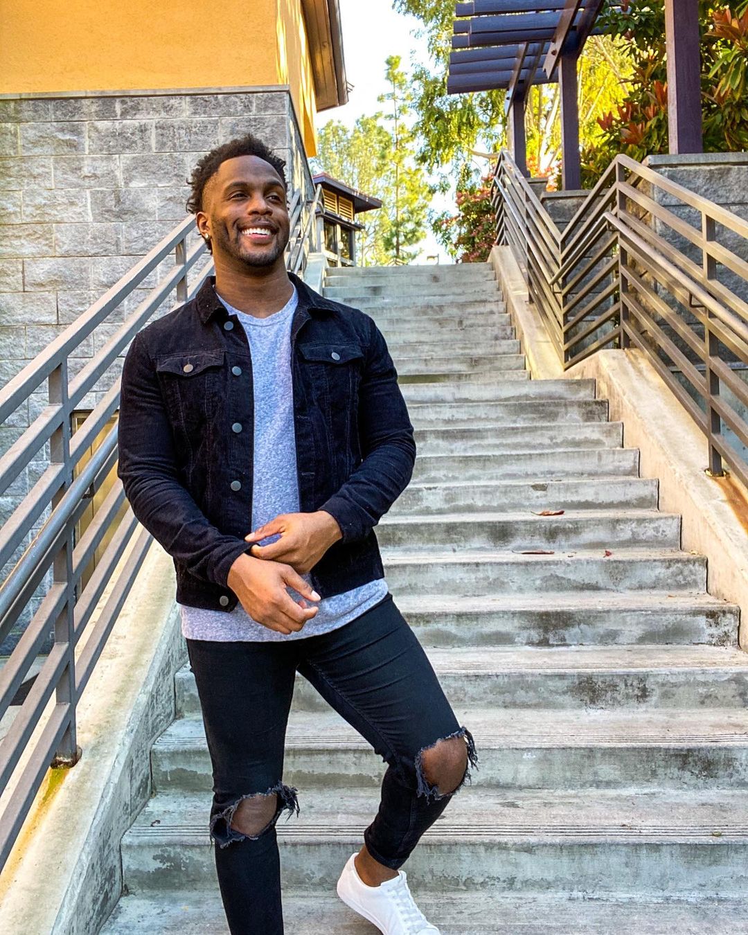 An incredible photo showing Uzoma Nwachukwu at the edge of a flight of stairs, rocking a ripped denim pant, gray inner shirt and black jacket.