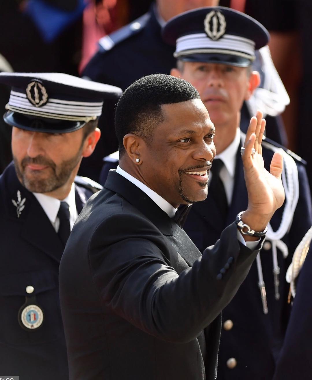 A photo showing Chris Tucker in a black tux paired with a white inner T-shirt as he waves to his fans.