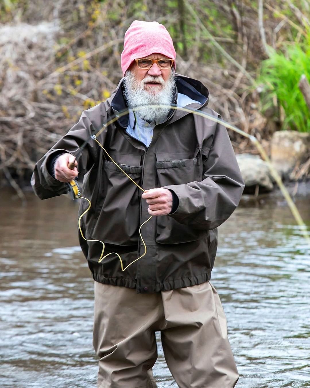 David Letterman goes fishing in a lake, in a brown coat and pant.