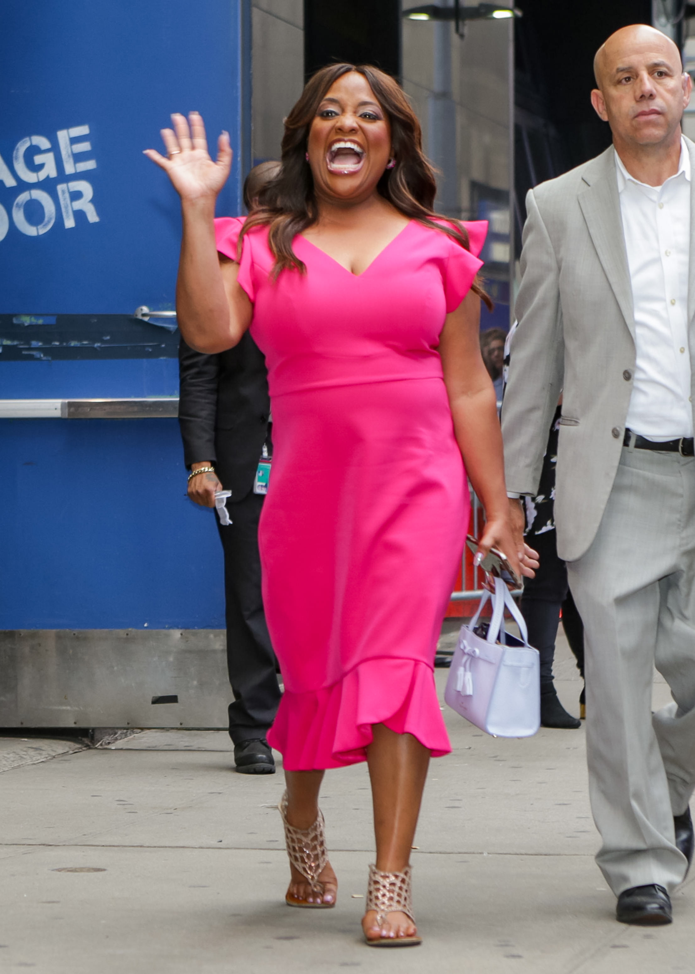 A photo showing Sherri Shepherd in a knee-length pink dress and basket design slippers, on the streets, with a white purse to match.