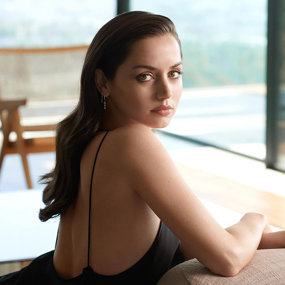 An amazing photo of Ana de Armas sitting on a couch in a black backless dress.