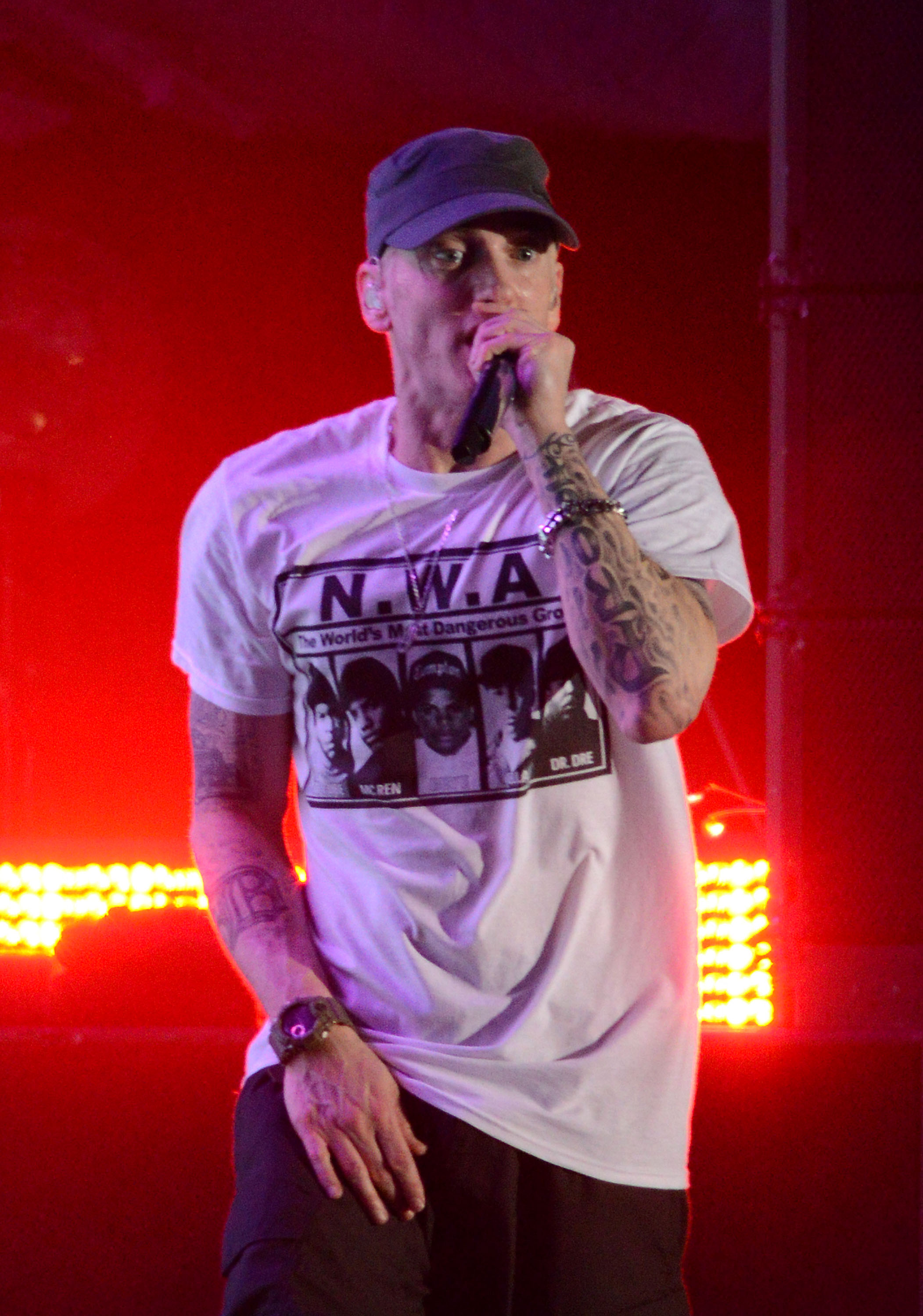 An image showing Eminem in a plain white Tee and black pant, performing on stage, with red lights in the background.