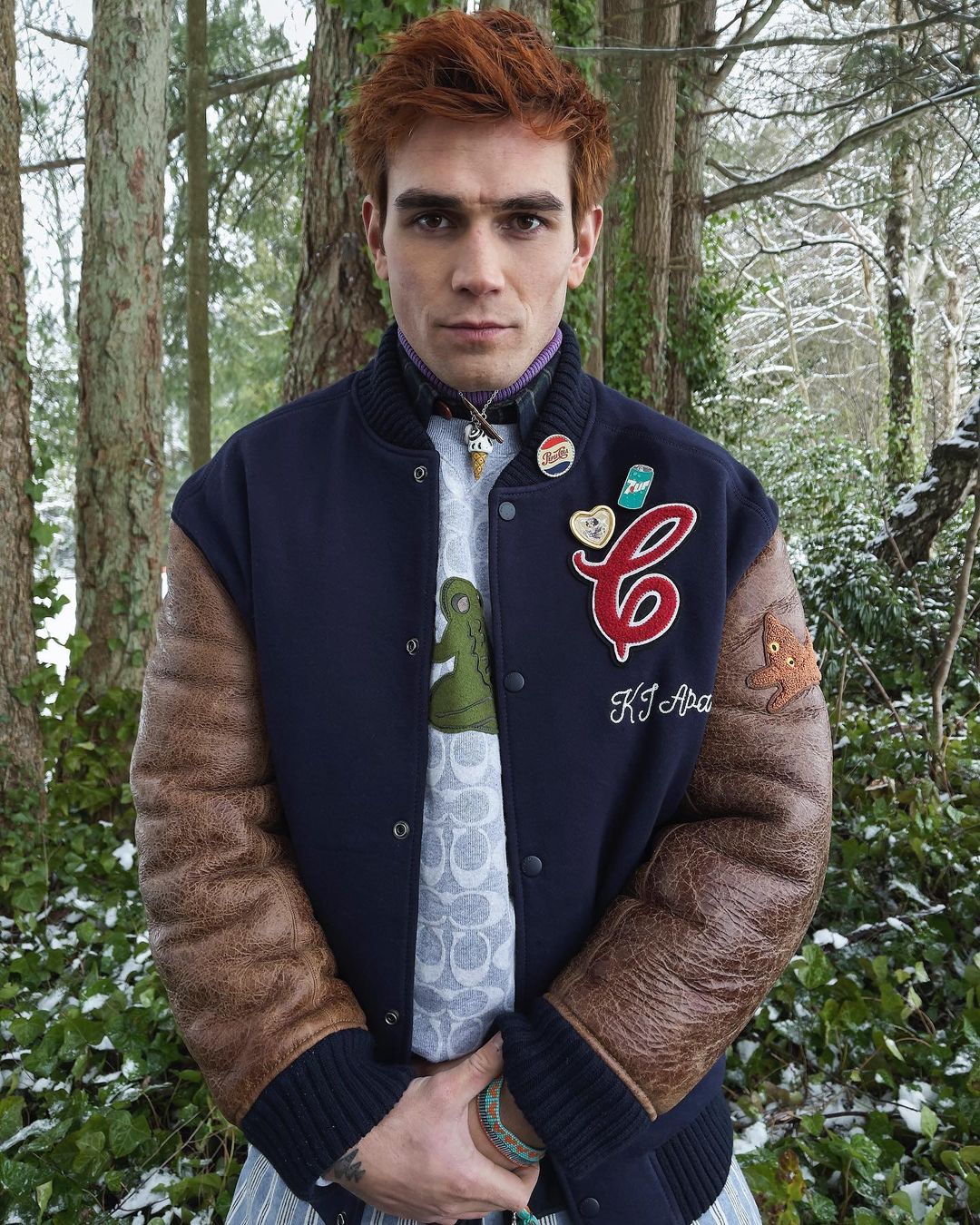 A photo showing KJ Apa in a varsity jacketin the woods.