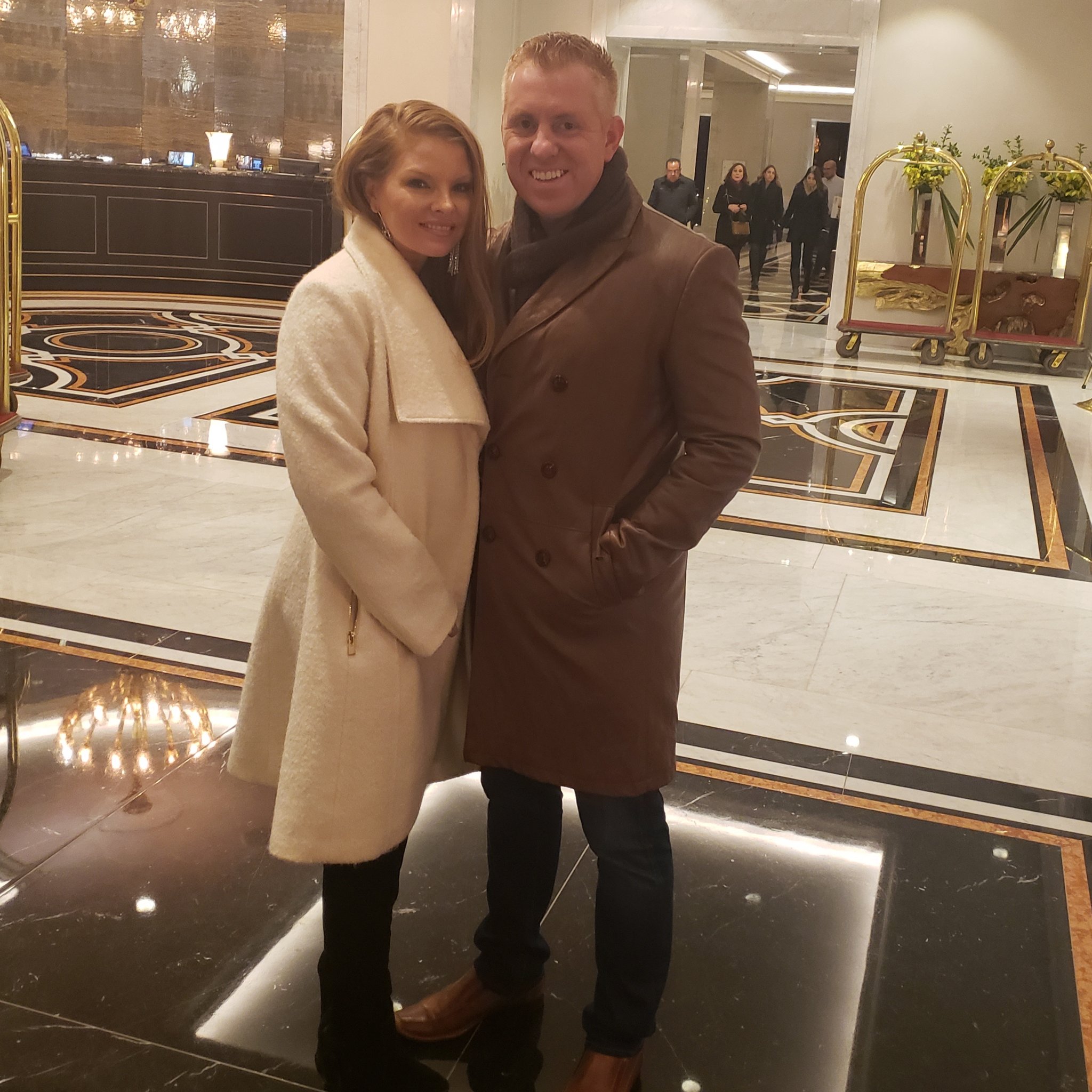 Bryan Redmond and wife Brandi wear long coats in a hotel lobby.