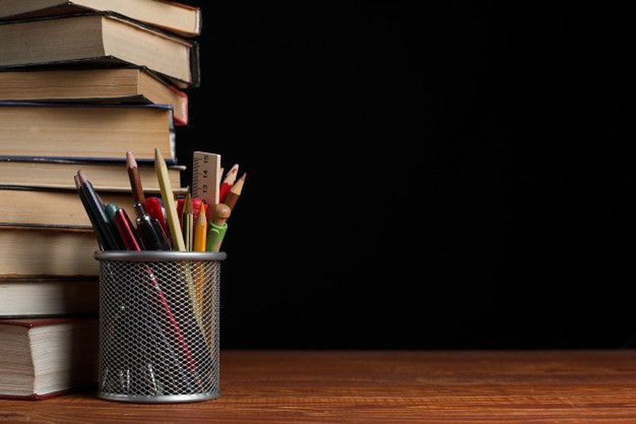A stack of classic books next to writing utensils on a desk