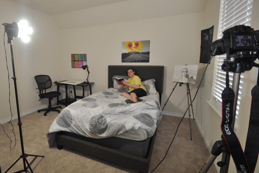 A bedroom set up for filming with camera and lighting equipment.