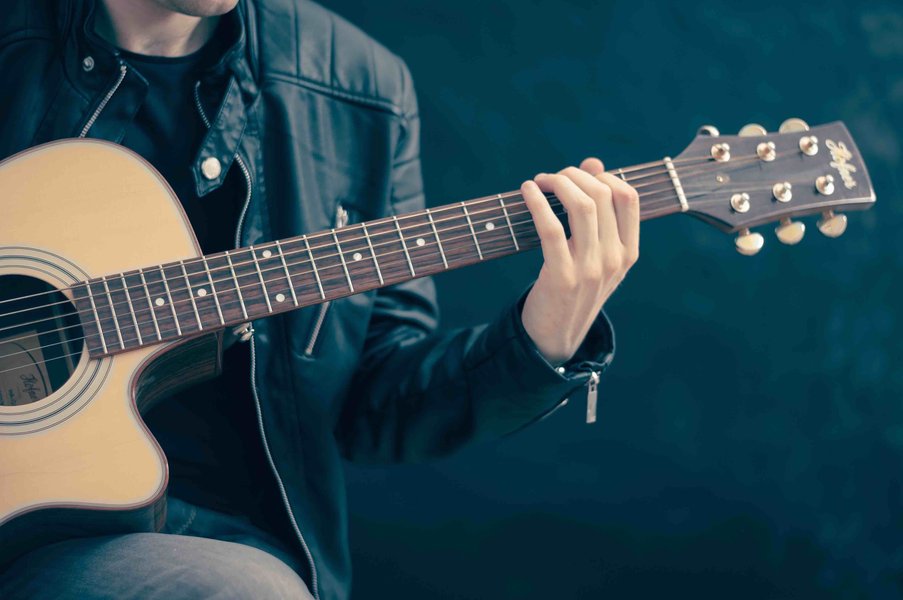 Close-up of hands holding a guitar neck, demonstrating fretting position.