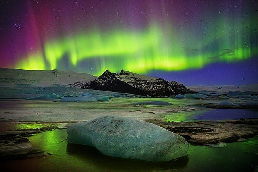 Bright green aurora over a reflective body of water in Iceland with mountains in the background