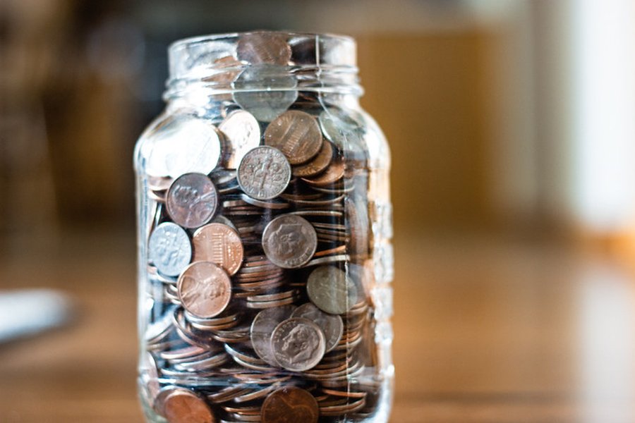 A clear glass jar nearly full of various coins, illustrating the concept of accumulating small savings.