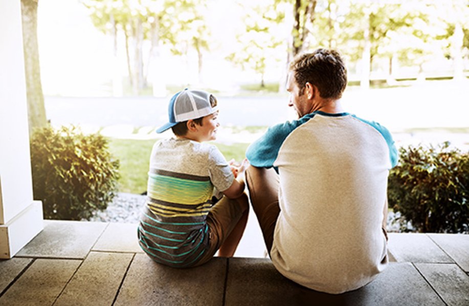 A father and son having a conversation on a porch, illustrating open communication.
