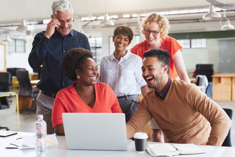 A diverse group of employees laughing and working together on a laptop.