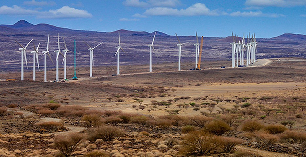Massive wind turbines spinning in a large field with a blue sky.