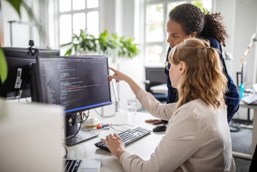 Two women collaborating on a coding project on a laptop.