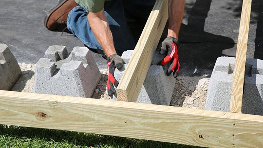 A close-up of a partially constructed floating deck frame with lumber joists and concrete blocks.