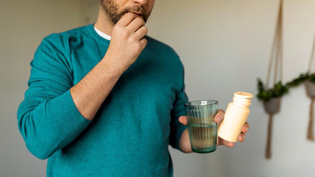 man taking supplement pills with glass of water