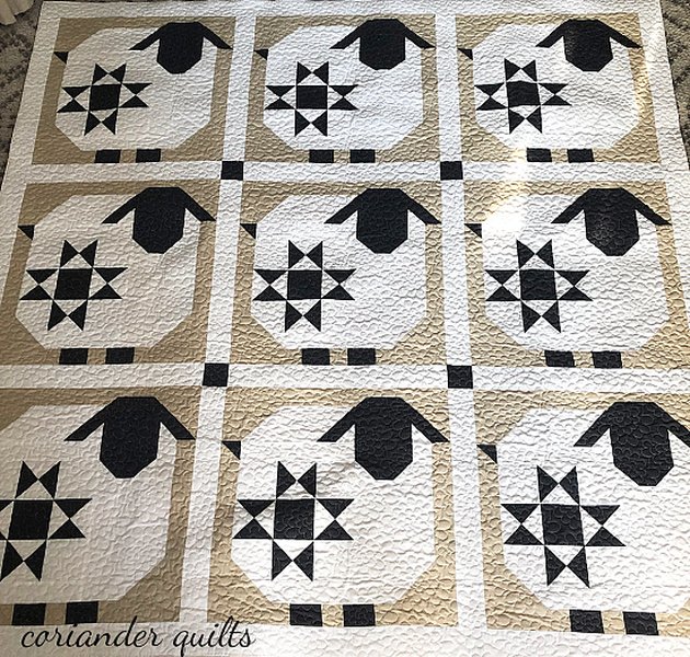 A quilt featuring multiple white sheep blocks with black faces and legs on a patterned background.