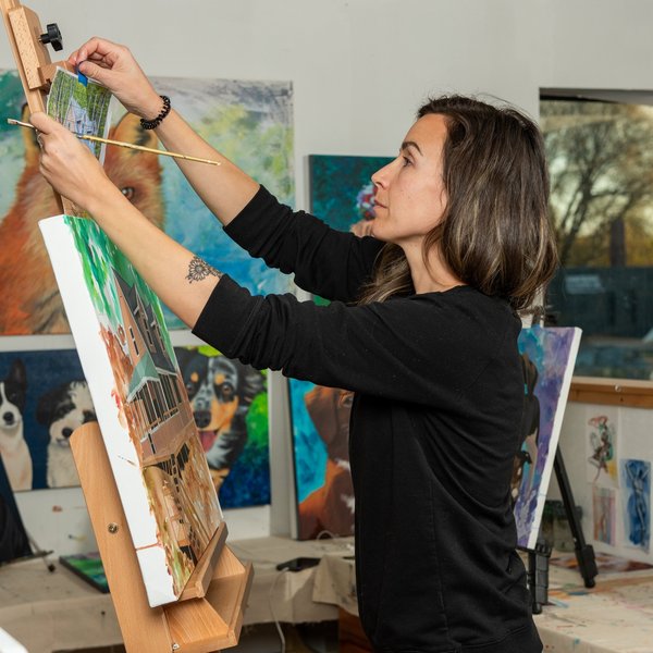 An artist working intently in her studio surrounded by supplies.