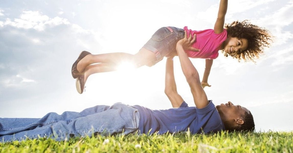 Father and daughter playing joyfully outdoors on a sunny day.