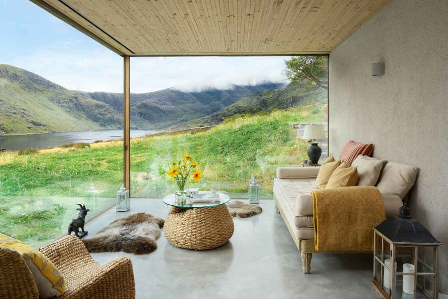 A modern living room with large windows overlooking a green landscape and a cozy seating area, illustrating prospect and refuge in interior design.