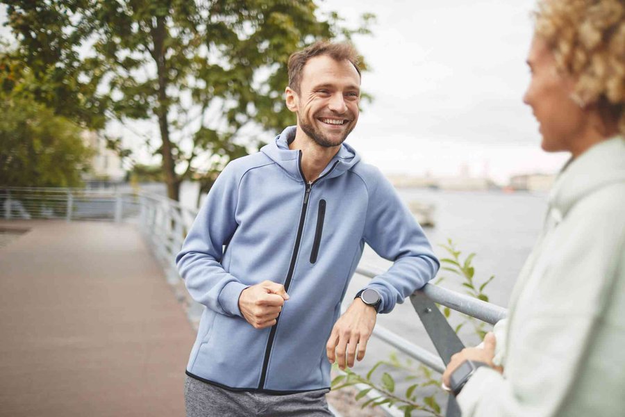 A man smiling warmly while talking to a friend outdoors, illustrating positive social interaction.