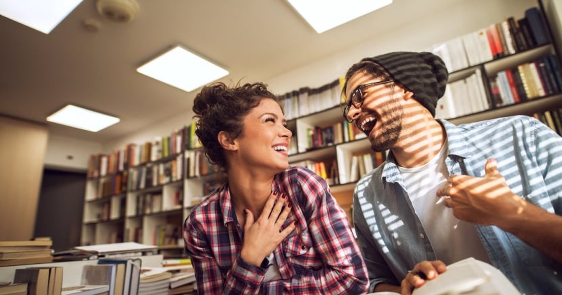 Two friends engaged in conversation and smiling in a modern library setting.