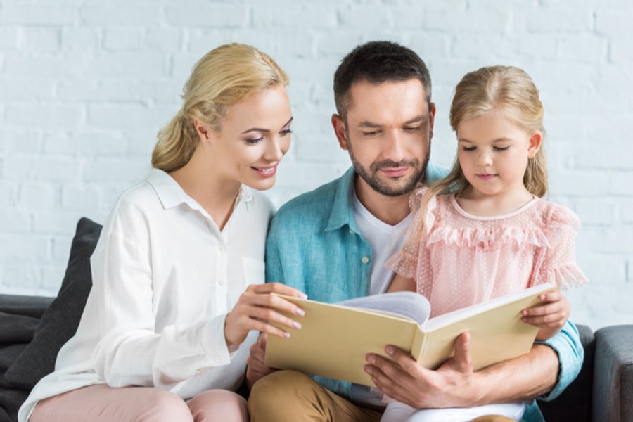 Parents helping a slightly older child with reading a book