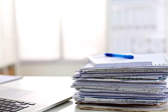 stack of research papers with notes and laptop