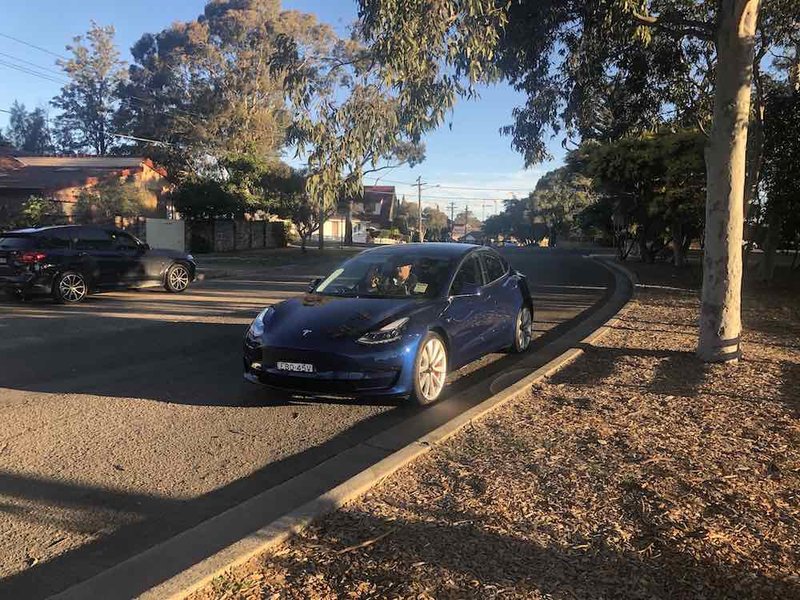 A Tesla Model 3 navigating suburban streets, where regenerative braking can boost efficiency.