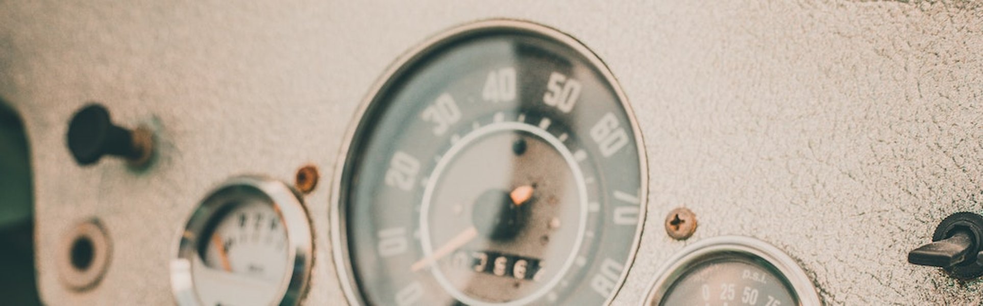 An image showing a car's odometer with hands holding a smartphone displaying a pay-per-mile app.