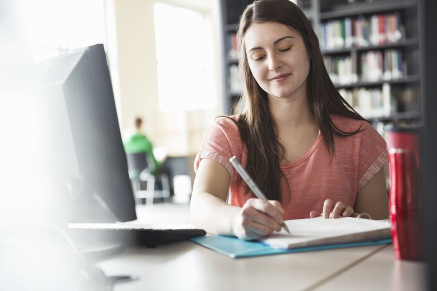 Student writing notes in a library setting