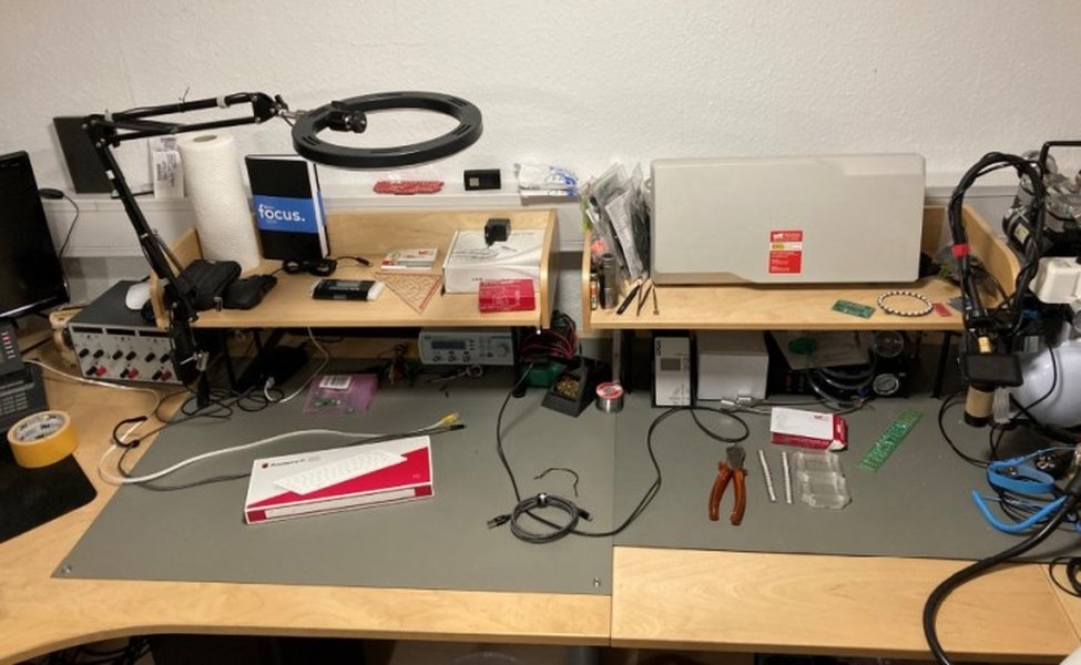 An engineer's workbench with embedded development tools, showing a microcontroller board, wiring, and a computer screen with code.