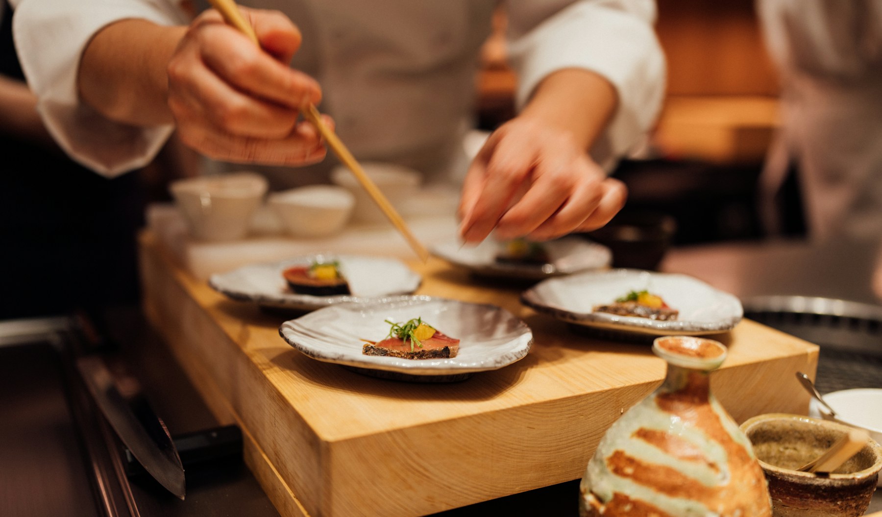 Hands plating a dish at the pass.