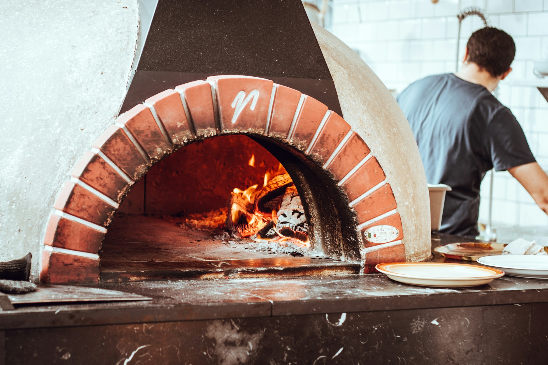 A chef at the white-oak oven, flames lighting the kitchen.