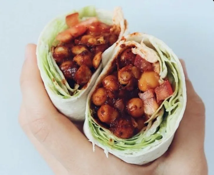 Two halves of a stuffed wrap on a plate showing a cross-section of smoky BBQ chickpeas, creamy avocado, crunchy slaw, and pickled jalapenos.