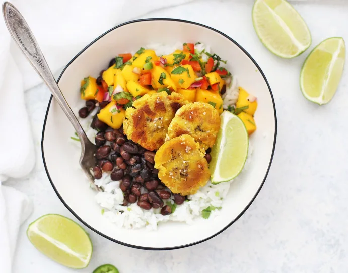 A colorful bowl of cilantro-lime rice topped with saucy black beans, golden caramelized plantain slices, pickled red onions, and a lime wedge.