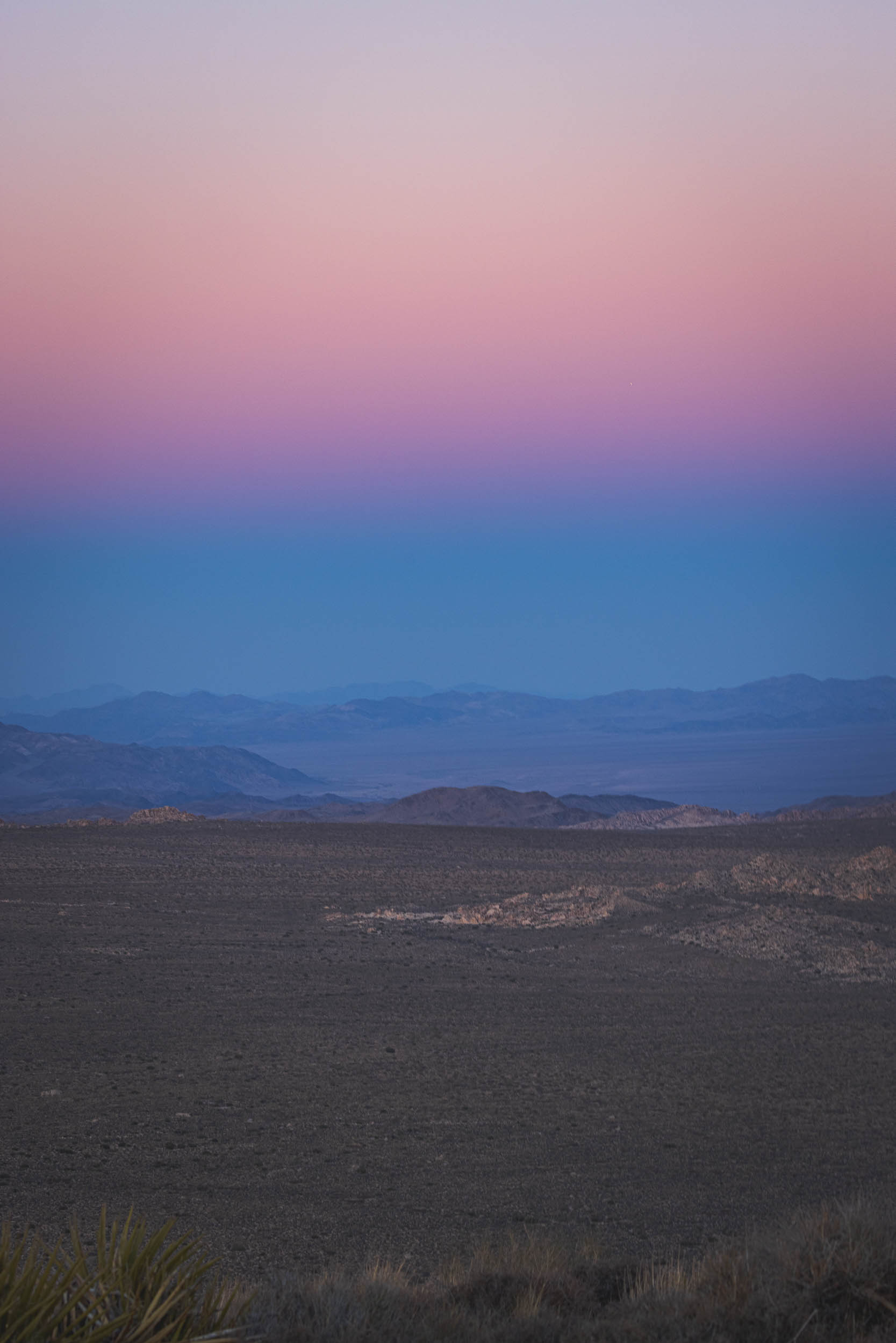 The shadow of the sunset as the sun dips below mountains in the distance
