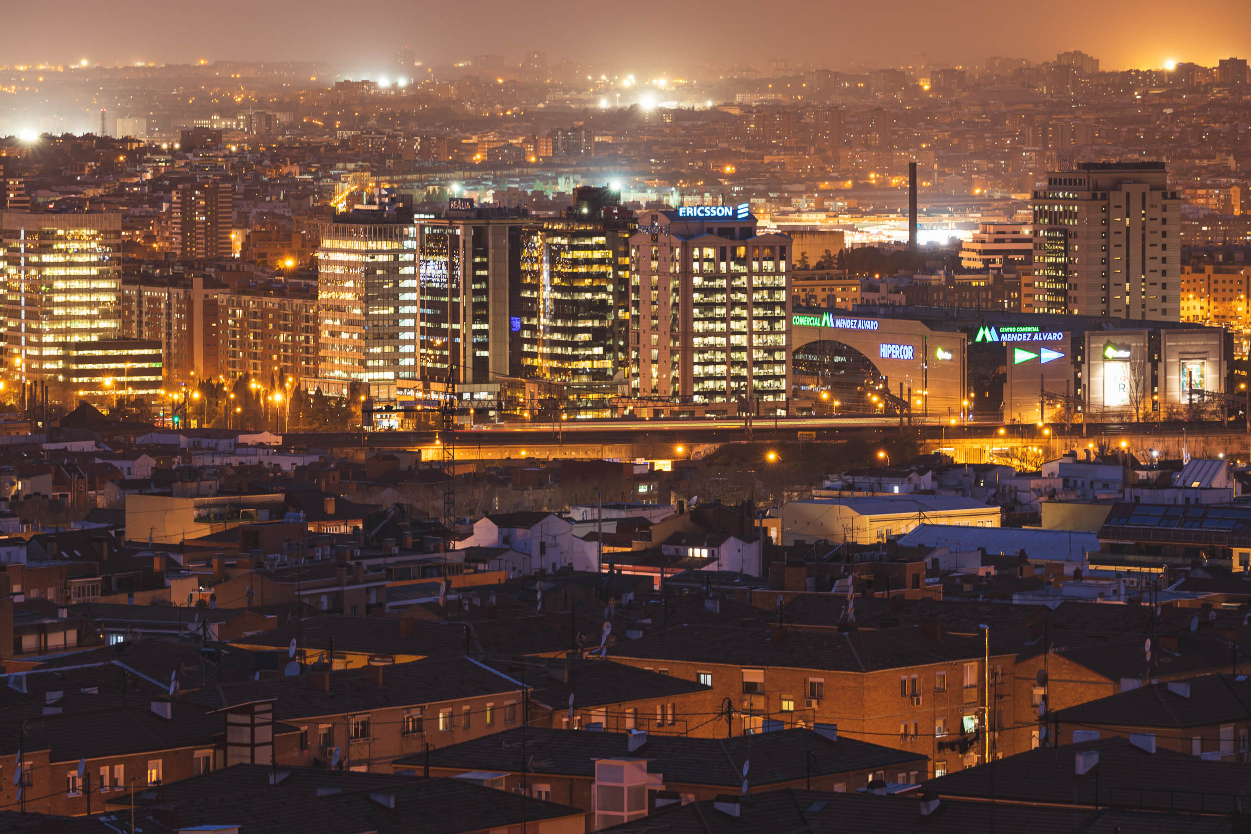 A train moves through rainy Madrid in the distance as buildings line the horizon.