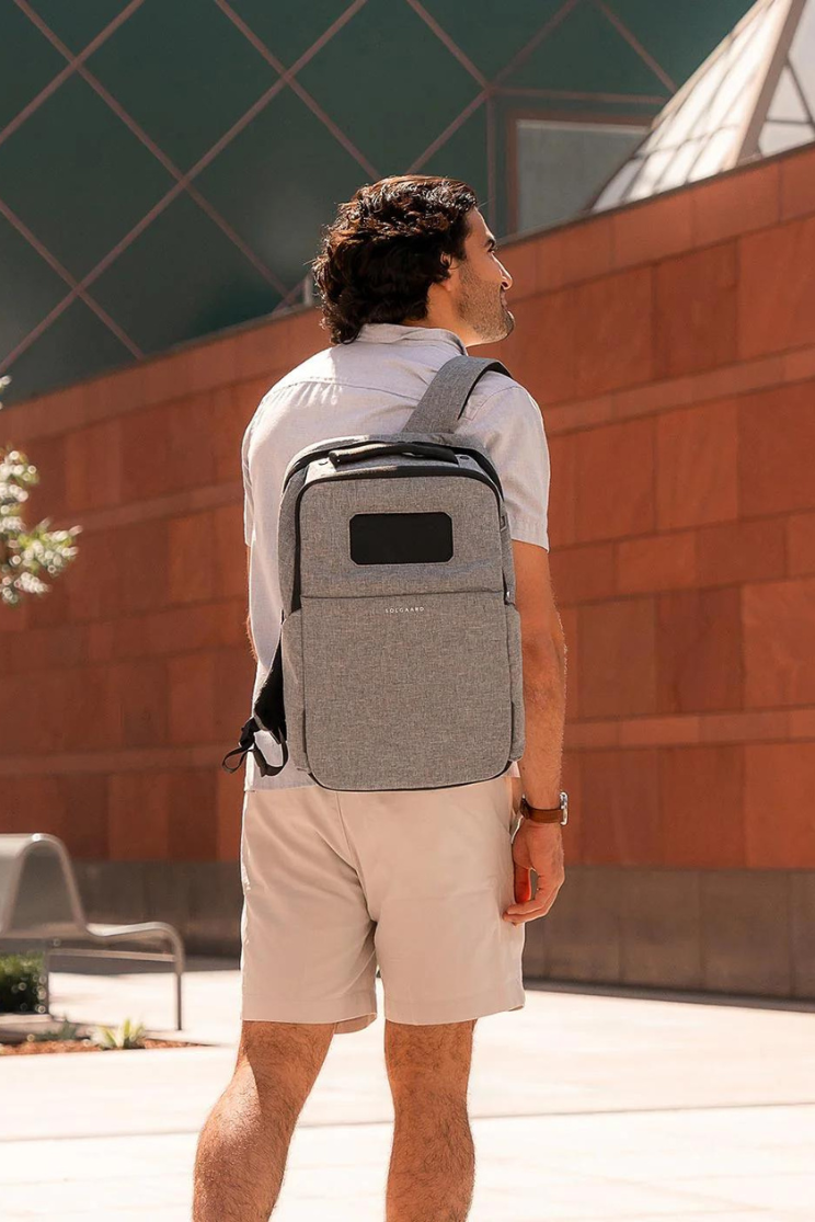 a person models a gray lifepack solar backpack, which has a black solar panel on the upper portion.