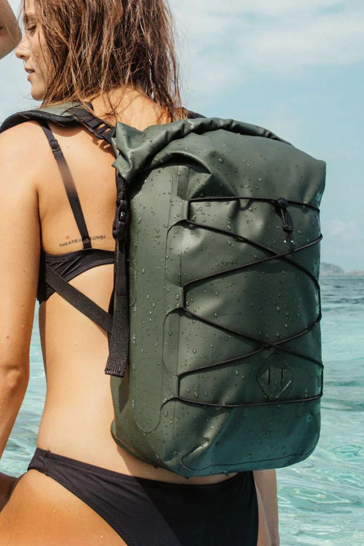 a person in a bikini with wet hair models the water proof daypack in green on the water.