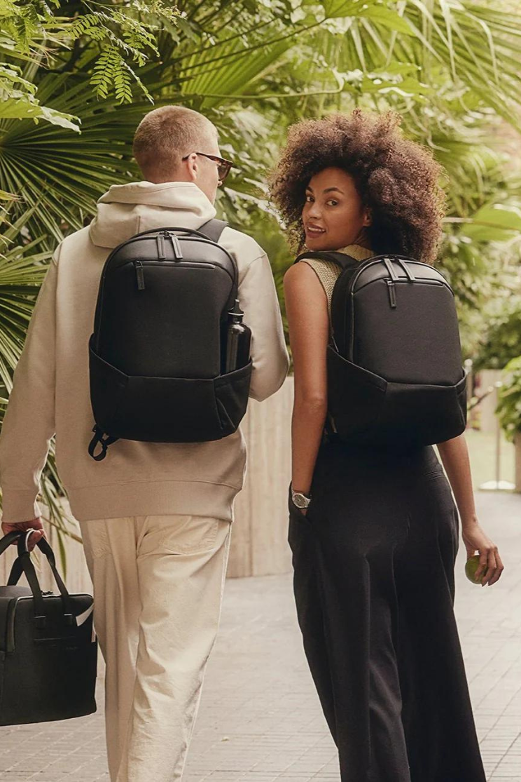 two people model compact apex backpacks outside. it has outer pockets for water bottles and two zippers at the top