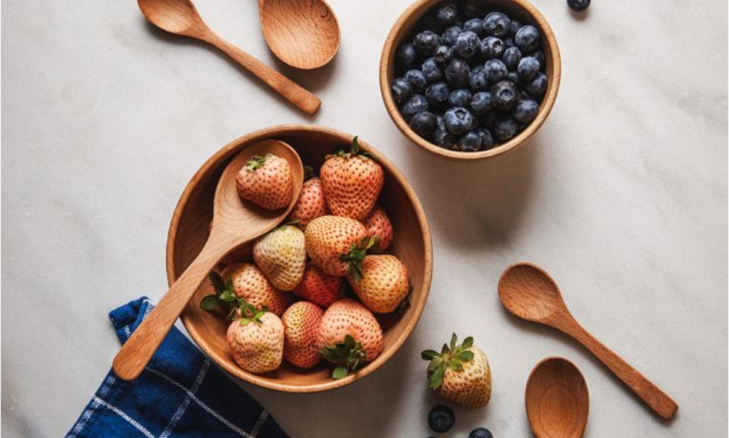 a collection of wooden spoons and bowls with strawberries and blueberries on a white countertop