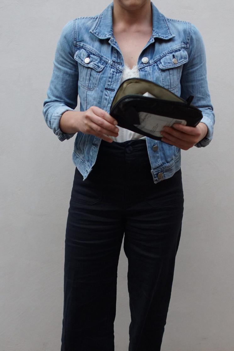 a person in a denim jacket and black pants holds a small black reusable mailer from limeloop