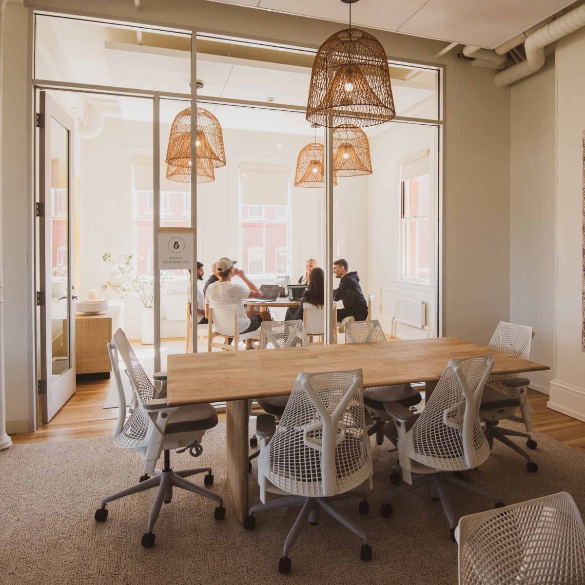 A small group of people working in a beautifully-lit office with tall interior windows