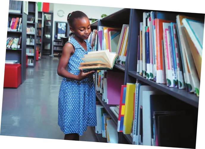 Imagem de uma menina segurando um livro em uma biblioteca.