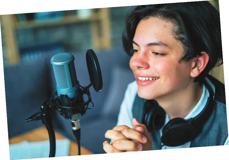 Imagem de jovem em frente a um microfone e com fones de ouvido pendurados no pescoço.