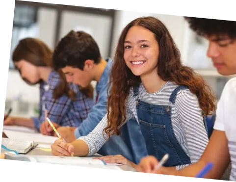 Imagem de quatro adolescentes em sala de aula escrevendo em seus cadernos.